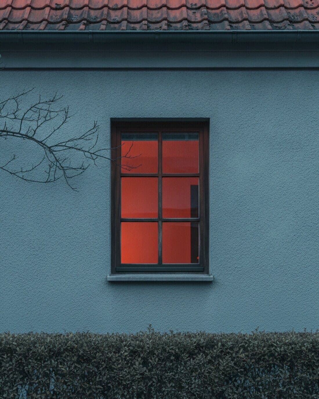 Hausfassade in der Abenddämmerung mit einem warm beleuchteten Fenster