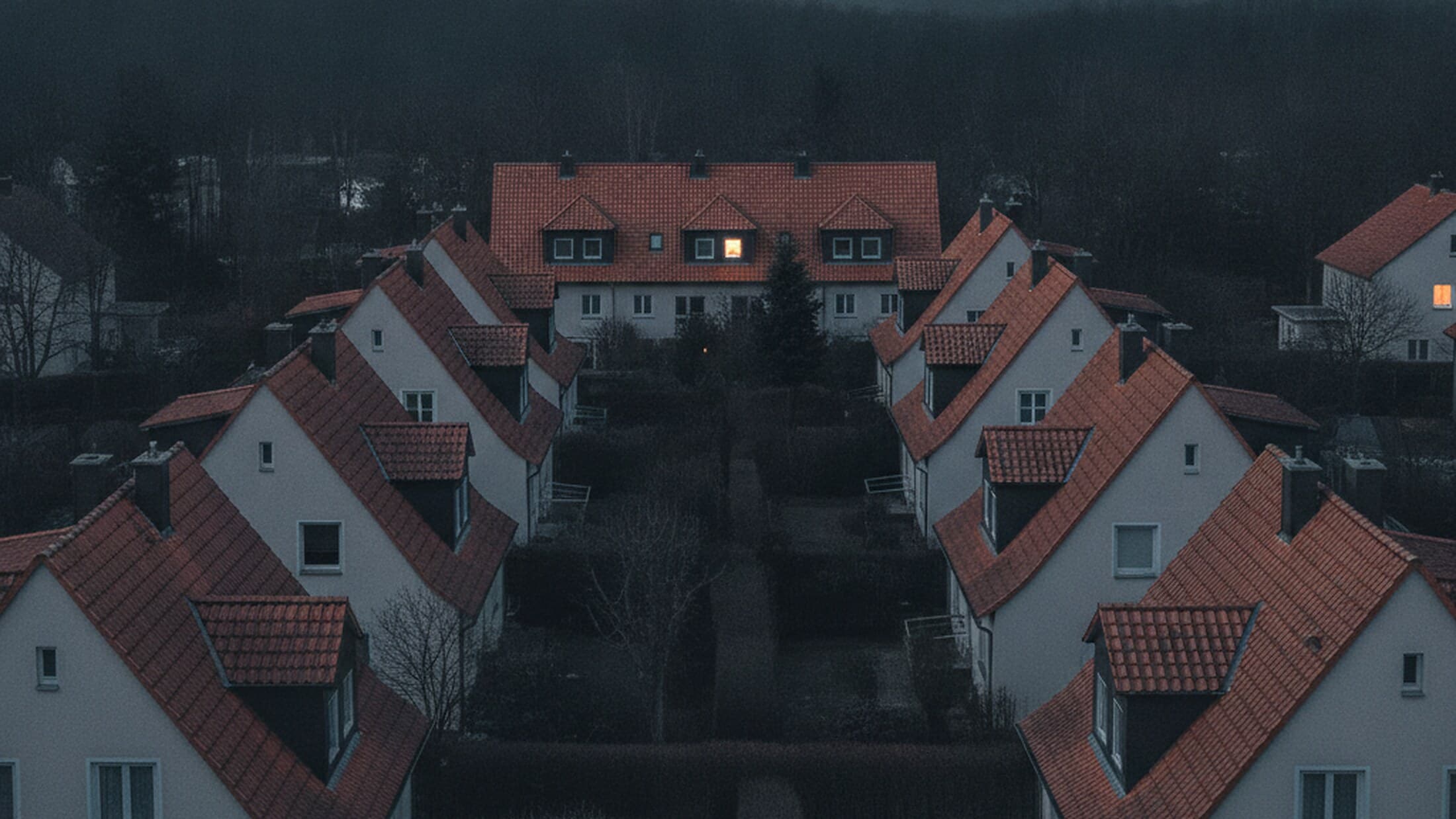 Wohnquartier mit Giebeldächern und einzelnen erleuchteten Fenstern in der Abenddämmerung