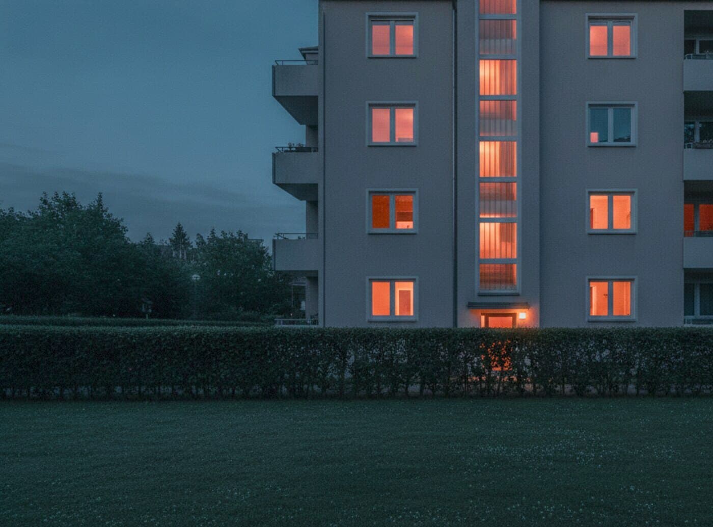 Viergeschossiges Wohnhaus mit verputzter Fassade und Treppenhausfenstern in der Abenddämmerung