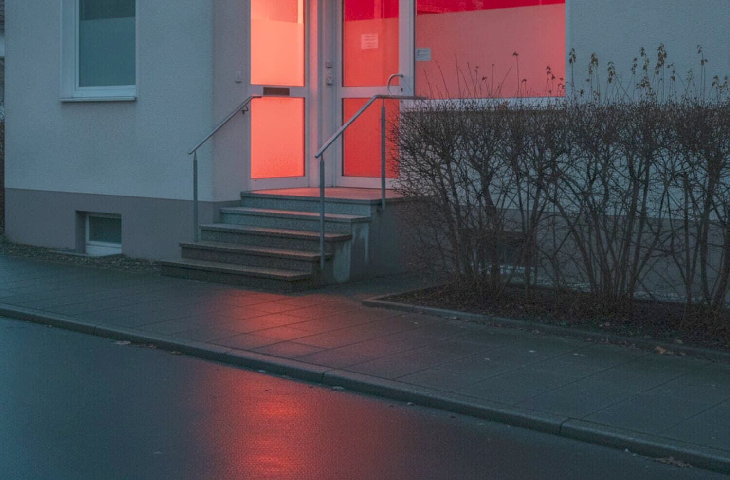 Eingang eines kleinen Erdgeschossbüros mit beleuchtetem Fenster in der Abenddämmerung