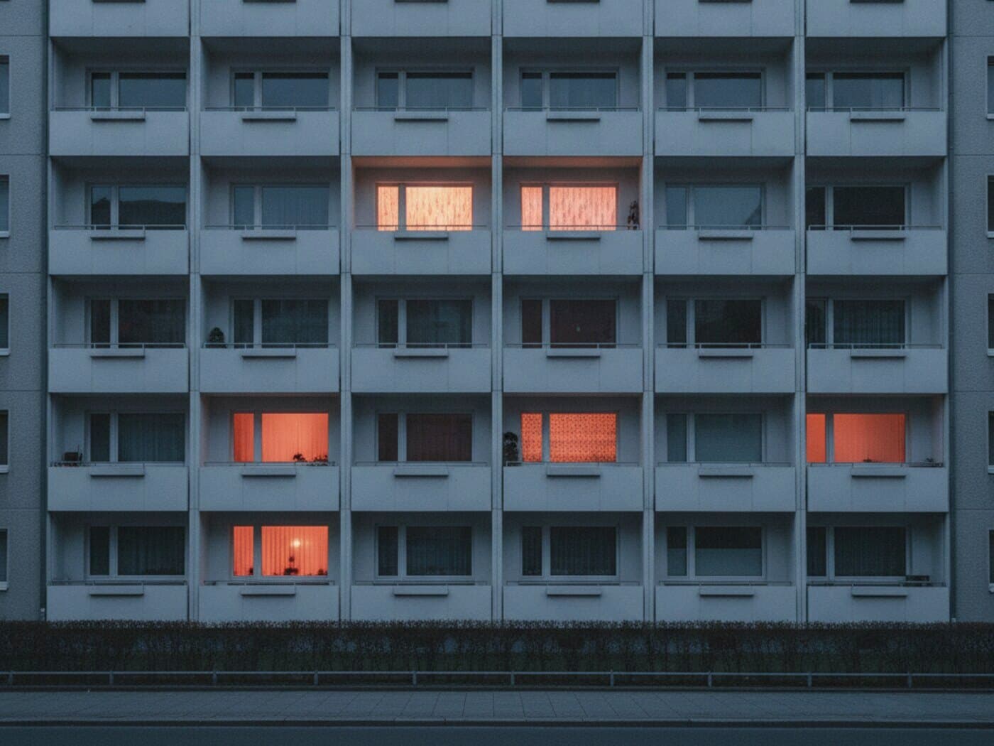 Fassade eines Mehrgeschossers mit Fensterraster, einzelne Wohnungen warm beleuchtet